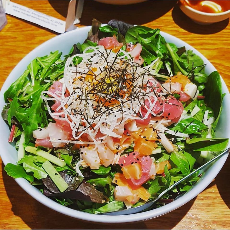 A vibrant poke salad with fresh tuna, salmon, and greens, topped with shredded daikon and nori.