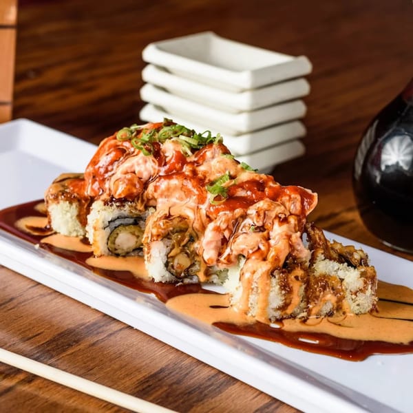 Sushi Cafe's fried shrimp tempura rolls topped with spicy sauce and green onions on a white plate.