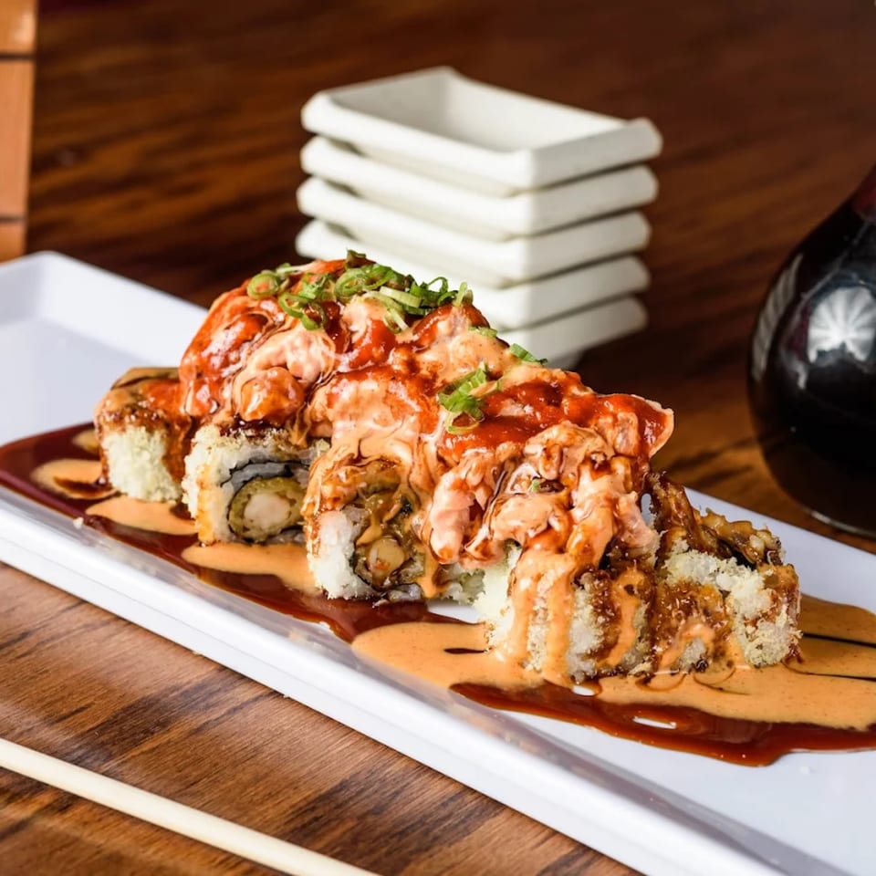 Sushi Cafe's fried shrimp tempura rolls topped with spicy sauce and green onions on a white plate.