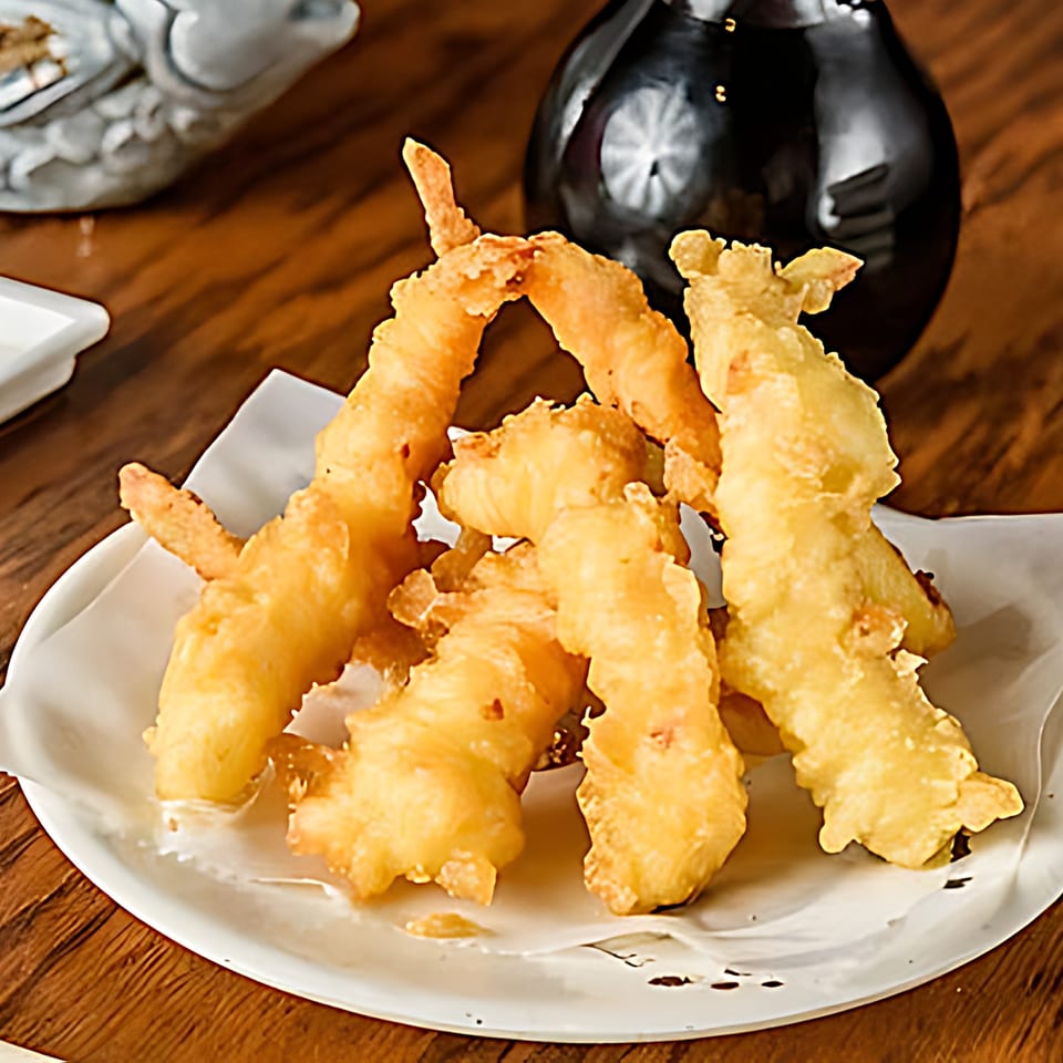 Golden-fried shrimp tempura on a white plate with a dark soy sauce bottle in the background.