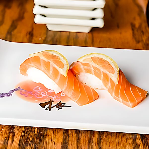 Two pieces of salmon nigiri sushi with lemon slices on a white plate with a decorative sauce.