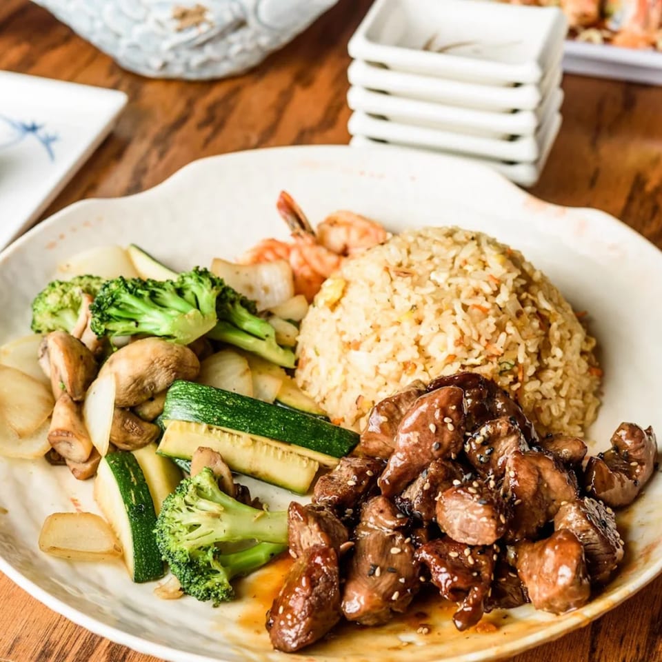 Japanese hibachi meal with steak, shrimp, fried rice, broccoli, zucchini, mushrooms, and onions.